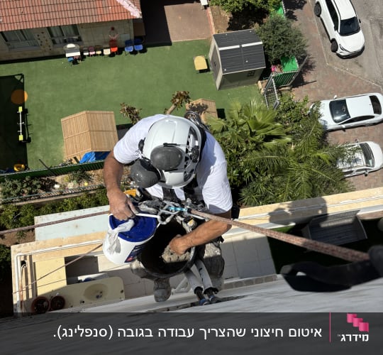 אדם בעבודת גובה על קיר בניין עם ציוד בטיחות